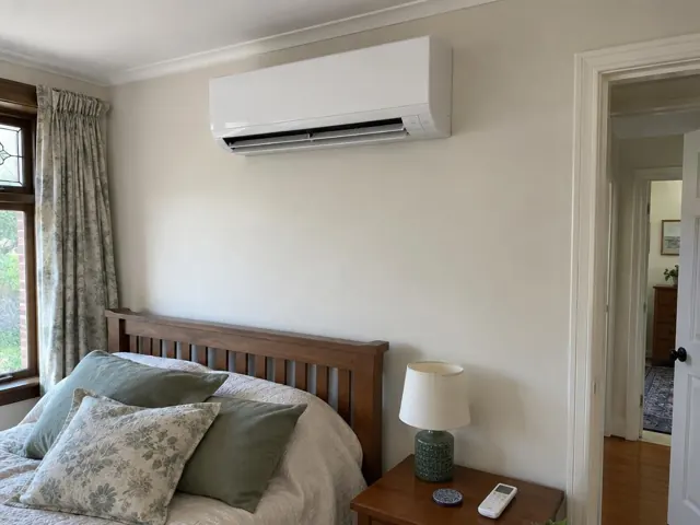 White wall split system above a wooden bed in a bedroom with window curtains in Blackwood