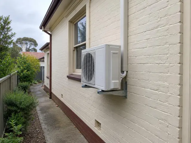 Outdoor air conditioner unit on a wall bracket beside a brick house window in Belair